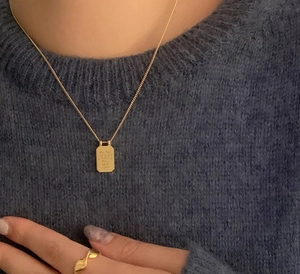 Detail of gold rectangular letter pendant necklace and wavy ring on navy sweater