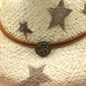 Detail of woven straw sun hat featuring brown star patterns and vintage bronze buckle