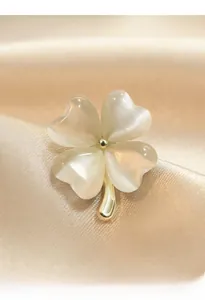 Macro detail of a four-leaf clover brooch with pearlescent petals and golden metallic stem