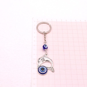 Detail of silver dolphin keychain with blue evil eye charms on a measuring grid