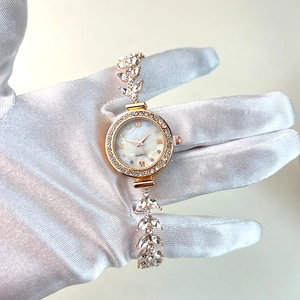 Detail view of gold watch with leaf-shaped bracelet and diamond-set mother of pearl dial