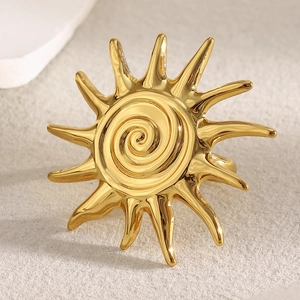 Detailed close-up of golden sun-shaped ring with spiral texture on a beige surface