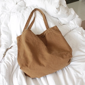 Vintage brown canvas tote bag with a soft texture placed on a white cozy bed setting