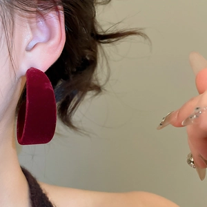 Gros plan d'un grand anneau en C en velours rouge porté par un mannequin de mode élégant