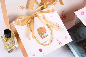 Detail of cartoon bear gift bag featuring golden silk ribbons and elegant packaging design