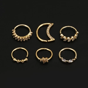 Set of 6 gold nose rings with star, moon and flower zirconia studs on black surface