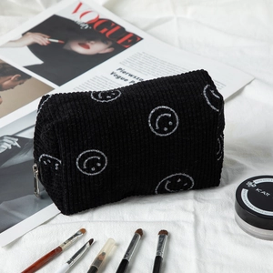 Detail of black corduroy makeup bag with white embroidered smiley face and silver zipper