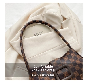 Close-up of brown monogram shoulder bag with wide strap on a white blazer background