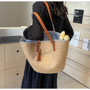 Detail of woven straw tote bag featuring blue striped lining and fringe tassel accent