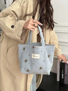 Light blue corduroy tote bag with bear embroidery held by a model in a beige coat