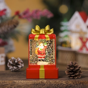 Close-up of a lit red Christmas gift box snow globe featuring Santa Claus and gold ribbon