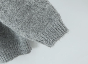 Detailed close-up of grey knit sweater showing soft plush texture and ribbed cuff design