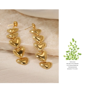 Detail of long hanging earrings with five tiered golden heart pendants on stone background