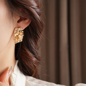 Close-up of golden irregular metal earrings with wrinkled texture on female ear