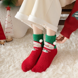 Detailed view of red Christmas coral fleece socks with Santa Claus pattern and white pom poms