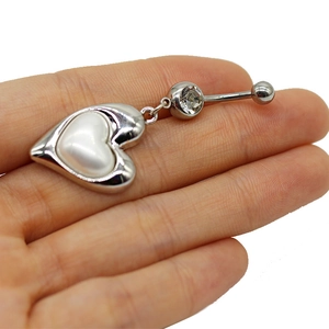 Macro view of silver heart navel ring with white inlay held in hand for size