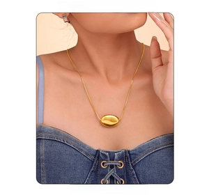 Detail of a layered golden snake chain necklace with an oval bean pendant on a model
