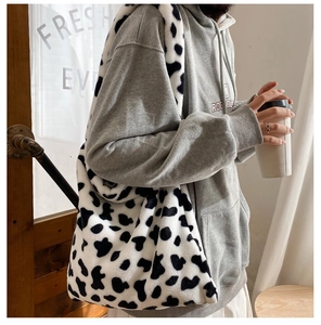 Spacious faux fur tote bag with cow print pattern shown on a shoulder in a cozy setting