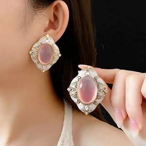 Vintage oval pink gemstone earrings with gold filigree and crystals on a black background