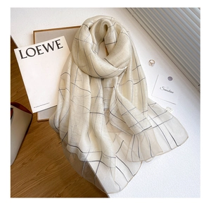 Macro detail of beige silk wool scarf with black pinstripe pattern on a sunlit table