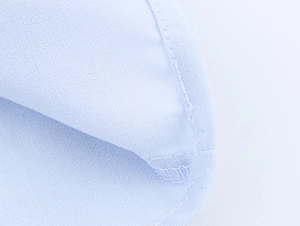 Close-up of light blue cotton fabric texture and precise overlock stitching on the shirt