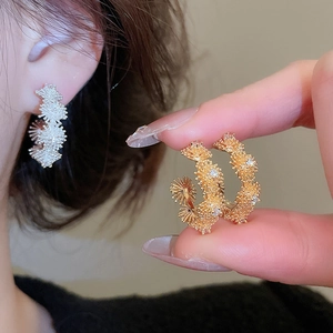 Detailed view of gold and silver C-shaped earrings with textured zircon flower pattern