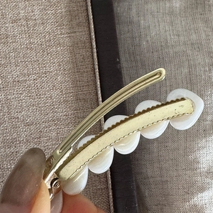 Detail of a gold metal hair clip with white resin hearts on a textured fabric