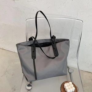 Detailed view of grey nylon tote bag with black slim straps on a transparent chair