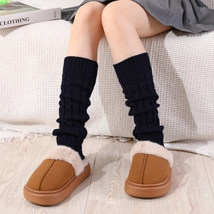 Close-up of black cable knit leg warmers paired with brown plush platform slippers