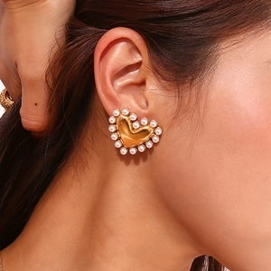 Close-up of heart-shaped gold earring with pearl trim worn on the earlobe