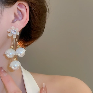 Détail de boucles d'oreilles fleur perle avec chaîne dorée portées à l'oreille