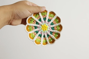 Close-up of handmade crochet coaster showing detailed colorful yarn weave and flower texture