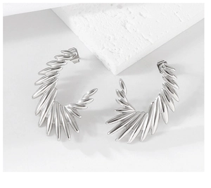 Macro detail of silver C-shaped wing earrings with radiant spiked edges on stone base