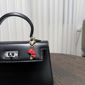 Detail of a red enamel mushroom keychain with gold chain on a black leather handbag