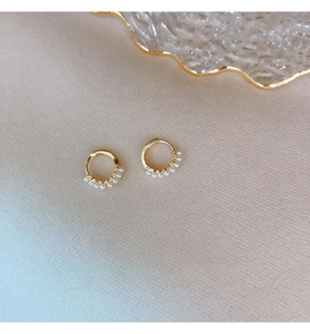 Detail of golden hoop earrings with small white pearls on a soft textured background