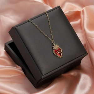 Detail of red heart necklace with gold crown in a black box on pink silk background