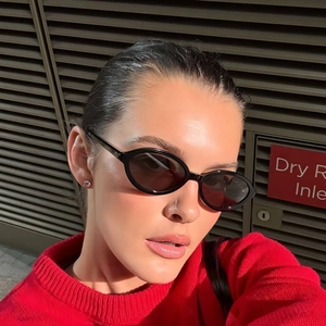 Fashionable black oval sunglasses for women with dark lenses on model against metal wall