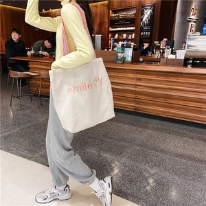Close-up of off-white canvas tote bag with pink smile embroidery and woven strap