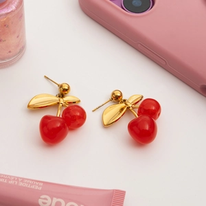 Detail shot of red cherry earrings with gold leaf accents on a white aesthetic background