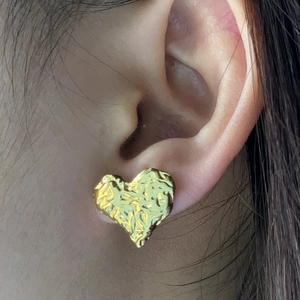 Gros plan sur un clou d'oreille cœur doré avec texture martelée porté par un modèle