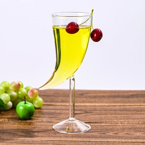 Close-up of a unique horn-shaped cocktail glass with cherries and yellow liquid drink