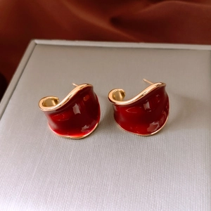 Macro view of C-shaped gold plated earrings with deep red enamel and wavy retro texture