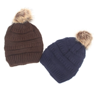 Detail of warm winter knit beanies in brown and navy with fluffy faux fur pom-poms