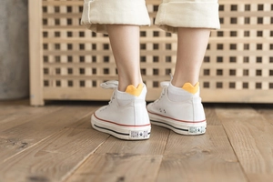 Detail of white low-top canvas sneakers and white ankle socks with yellow heart on the heel
