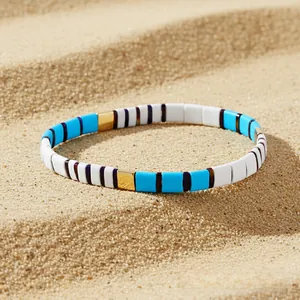 Detailed view of colorful enamel square beads bracelet resting on ripple sand