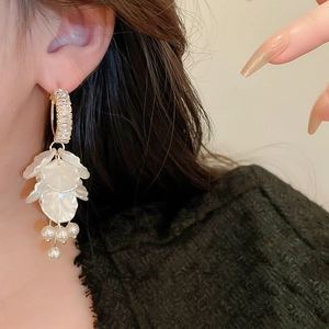 Close-up of dangling pearl tassel earrings with gold C-hoop and white petal shells