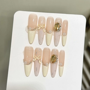 Detail of cream press-on nails with white bows, pearls and champagne gold rhinestones