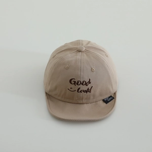 Detail of embroidered Good Luck lettering and smiley face on khaki cotton baby baseball cap