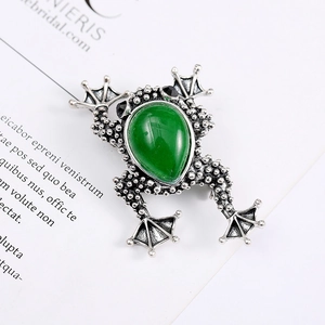 Macro shot of retro frog brooch with green teardrop stone and detailed vintage metal texture