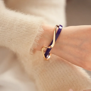 Detail of double-layer geometric cuff bracelet in gold and purple over a soft sweater